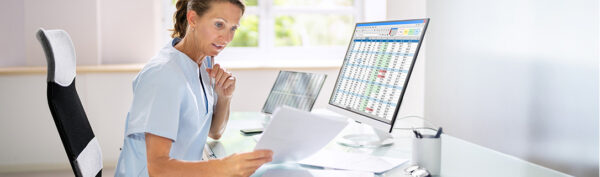 Female doctor looking at papers while sitting at a computer.